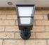 Modern dark gray outdoor wall light with integrated sensor on a brick facade.