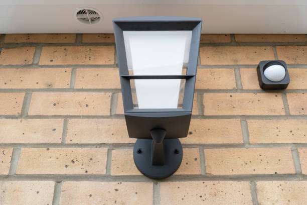 Modern dark gray outdoor wall light with integrated sensor on a brick facade.