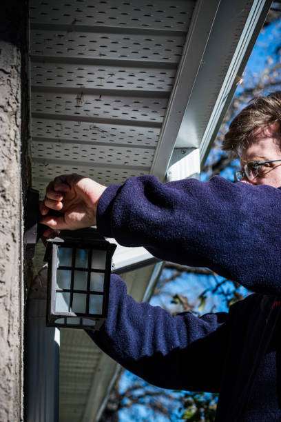 Man installing outdoor solar light by house exterior.