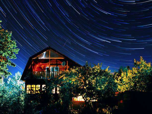 Home at night under a sky full of star trails, enhanced by a decorative wall light.