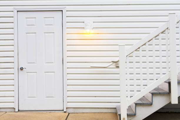 Outdoor wall light illuminates a white door on a siding wall with stairs.