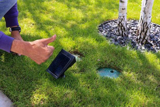 Hands installing small outdoor solar light in grass.