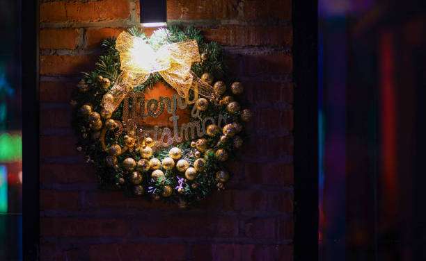 Festive Christmas wreath with gold ornaments illuminated by a black Wall Light on brick.